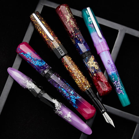 BENU fountain pens with glittery clear resin barrels in gold and multicolor tones on a dark background