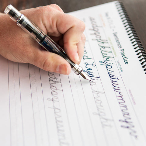 Hand using a fountain pen to practice cursive writing in a spiral notebook