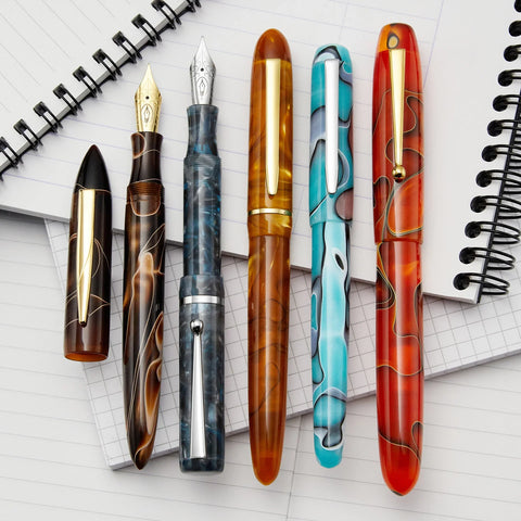 Colorful fountain pens with a background of open notebooks