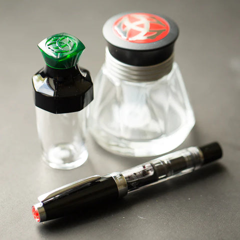 Two ink bottles with colored caps and a black fountain pen on a gray surface