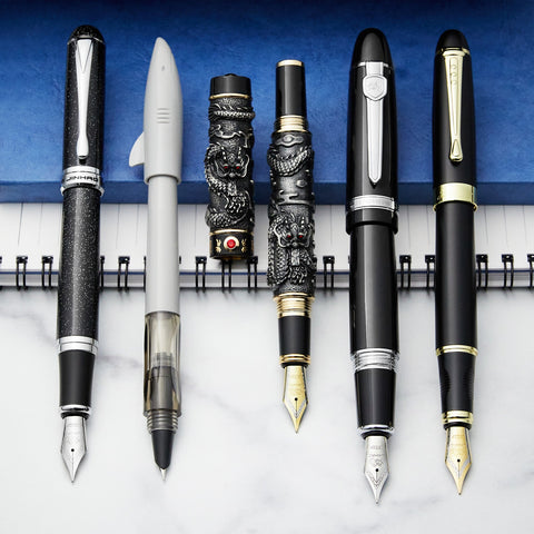 A group of black and grey fountain pens on a blue and white background