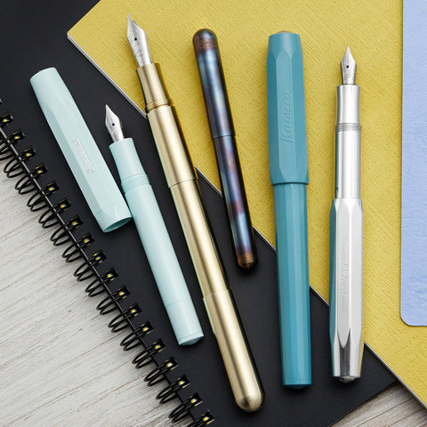 A group of colorful fountain pens on a stack of noteboks
