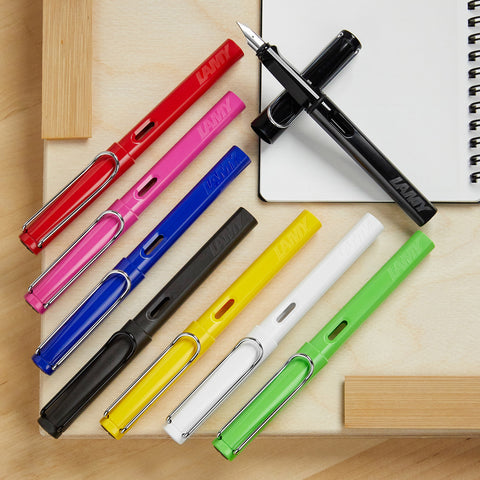Colorful converter fountain pens in red pink blue black and yellow arranged across a notebook.