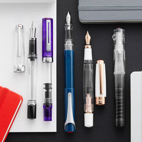 TWSBI fountain pen collection with silver, purple, and blue pens set against a dotted notebook page