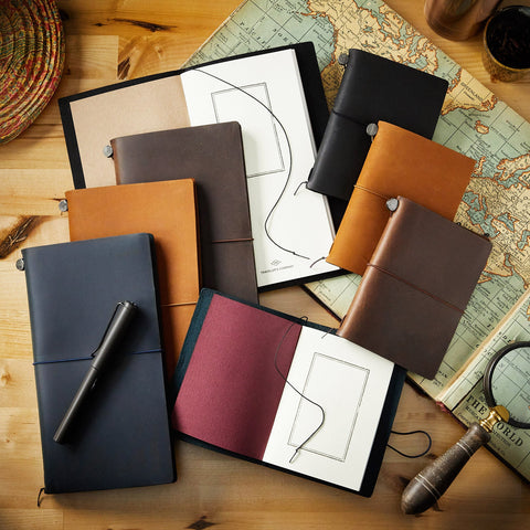 Traveler's Company notebook collection spread on a wooden desk with leather covers and a map sheet