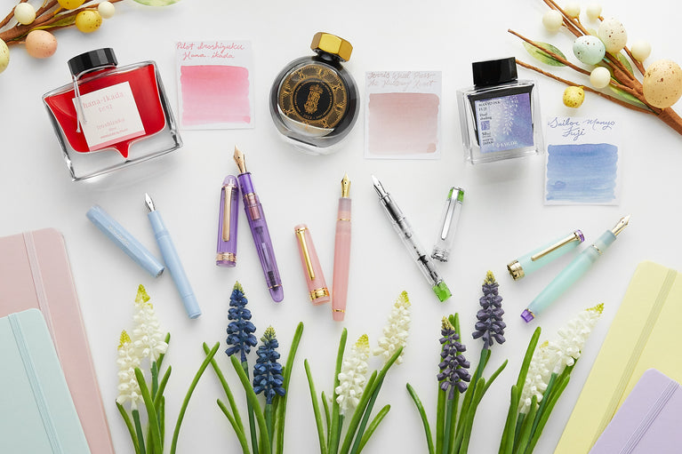 Spring pastel colors of fountain pens, ink, and notebooks with flowers and speckled eggs