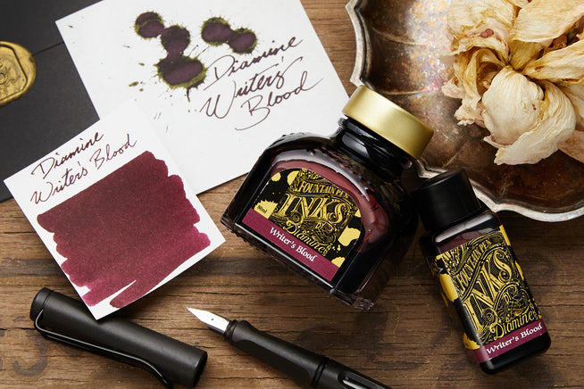 Diamine Writer's Blood fountain pen ink bottles with swab and writing samples on wooden background