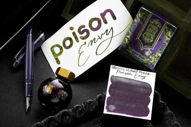 Purple Fountain pen with cap off, glass bottle of Ferris Wheel Press Poison Envy Fountain Pen Ink, box for the ink, and two white cards with writing and a swab on them, respectively, all on black background