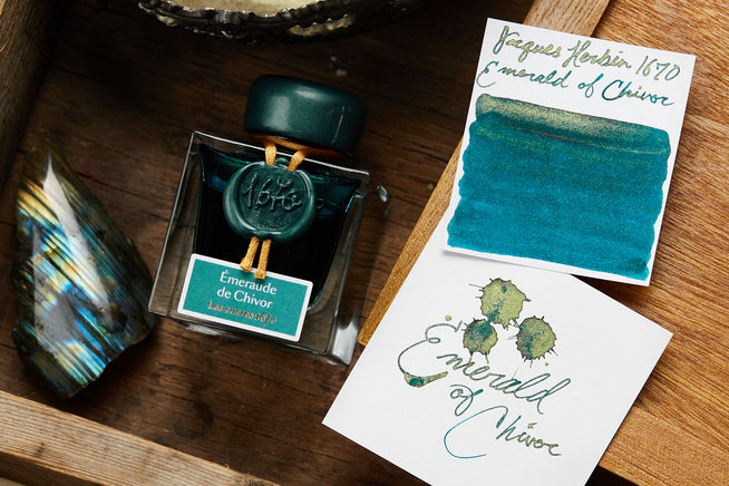 Jacques Herbin Emerald of Chivor ink bottle on desk with ink swab and writing sample