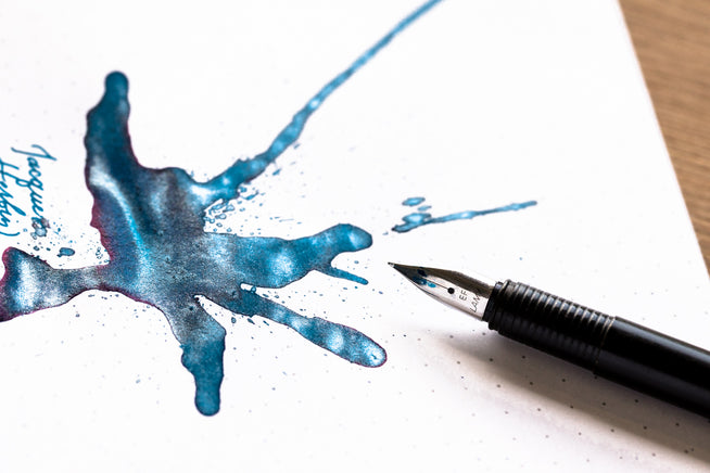 Shimmering teal blue ink splatter with an uncapped fountain pen