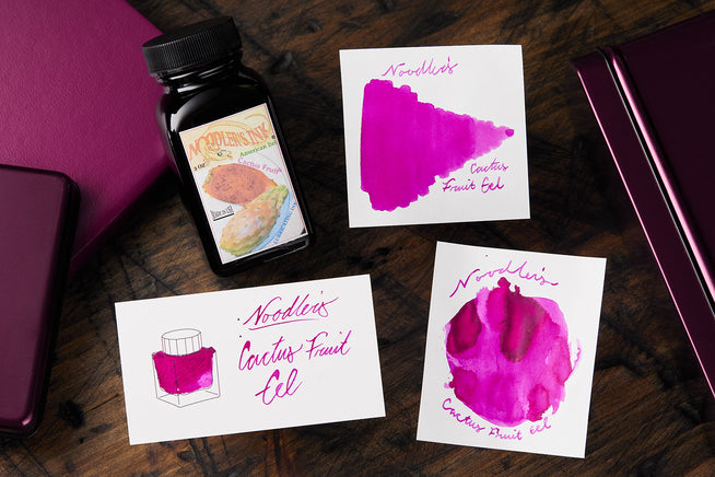 Noodler's Cactus Fruit Eel fountain pen ink bottle, and 3 swatch cards on wooden desk background
