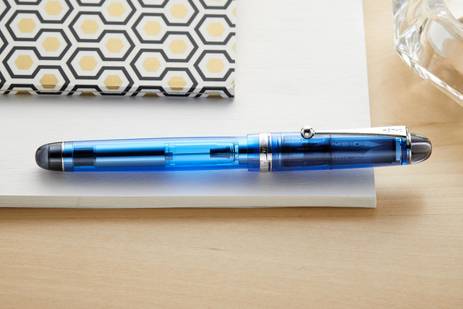 Pilot Custom 75 fountain pen,blue, on white notebook on light wood desk background