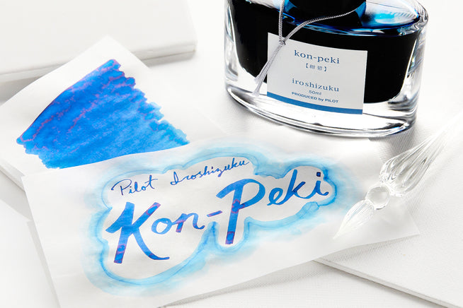 Bottle of Pilot Iroshizuku Kon-Peki fountain pen ink with swab and swatch on white paper with white background