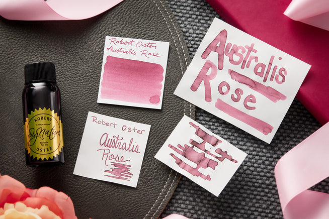 Robert Oster Australis Rose fountain pen ink bottle with writing samples on dark background with a ribbon and rose.