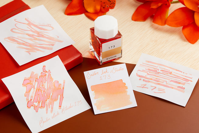 Sailor Ink Studio 173 Fountain Pen ink bottle, writing sample and swabs on wood, orange and cream background
