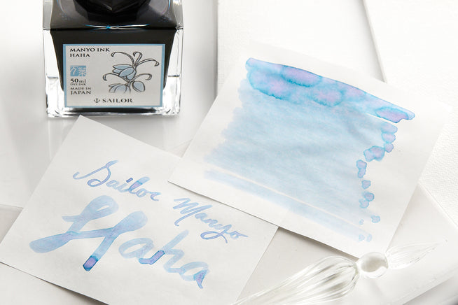 Bottle of Sailor Manyo Haha fountain pen ink with swab and writing, on a white piece of paper and white background. 