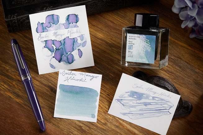 Sailor Manyo Hinoki fountain pen ink bottle, swab and writing sample on wooden background