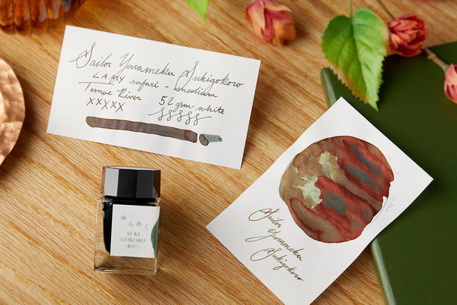 Sailor Yurameku Sukigokoro Fountain Pen ink bottle, with swab and writing sample on wooden background
