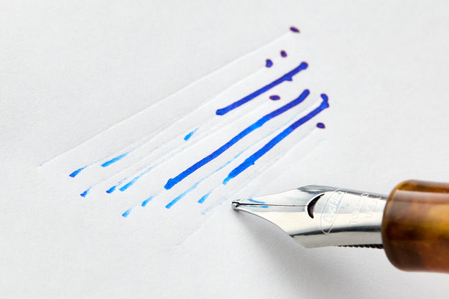 Blue lines of ink on white blank paper withj close up of a nib in an orange grip section