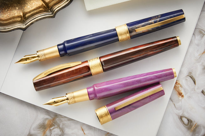 Visconti Mirage Mythos fountain pens in blue, brown and purple on white paper on top of a marble background