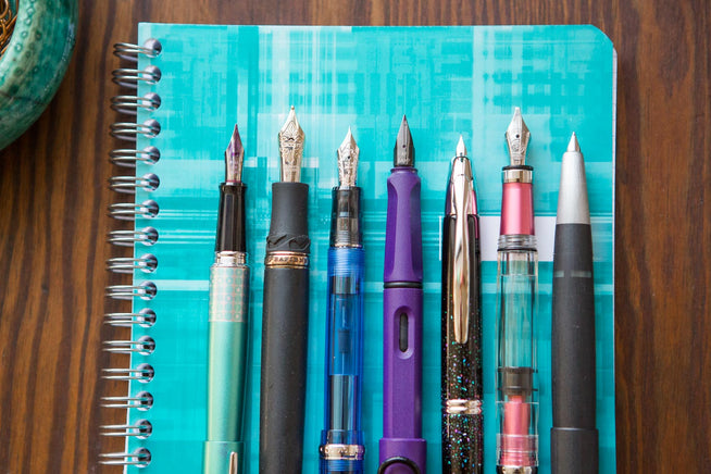 Assorted fountain pens uncapped on turquoise Clairefontaine notebook