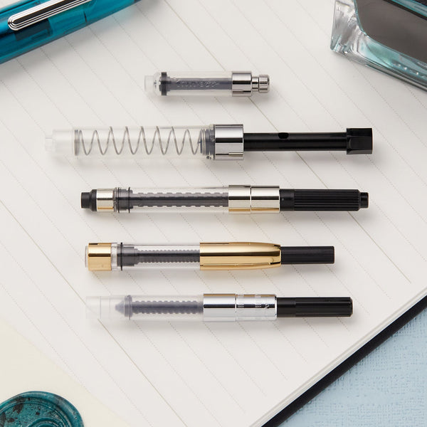 Assorted fountain pen parts including barrels nibs and sections arranged on a notebook.