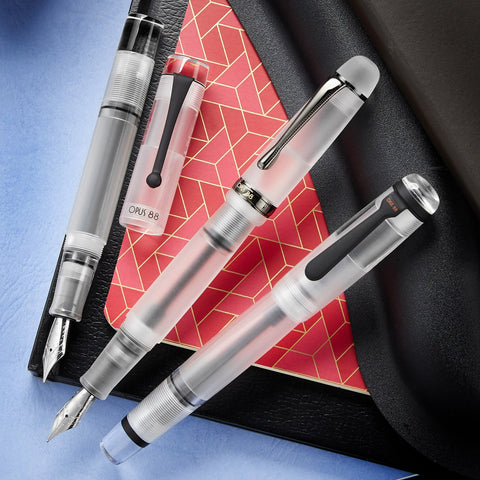 Three clear fountain pens on a colorful background
