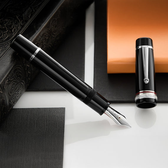 A close-up of a solid black fountain pen with silver trim and a decorative silver band around the cap.