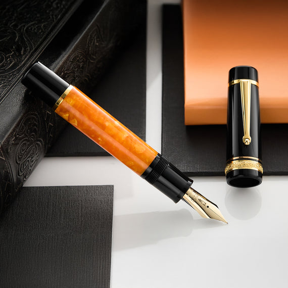 This oversized fountain pen features a black cap and an orange marbled resin barrel with black and gold trim.