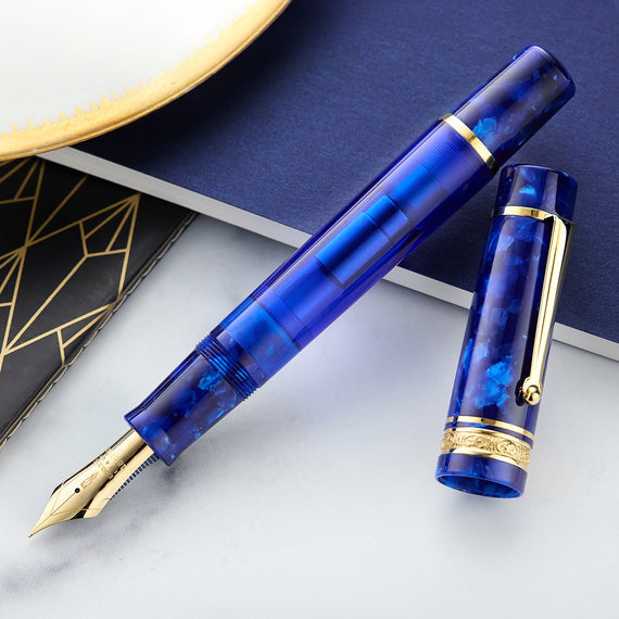 This image features a Delta DV Original Mid-Size Fountain Pen in Imperial Blu, a limited edition model. The pen has a stunning blue finish, 24k gold-plated trim, and an oversized #8 JoWo 18k gold nib.
