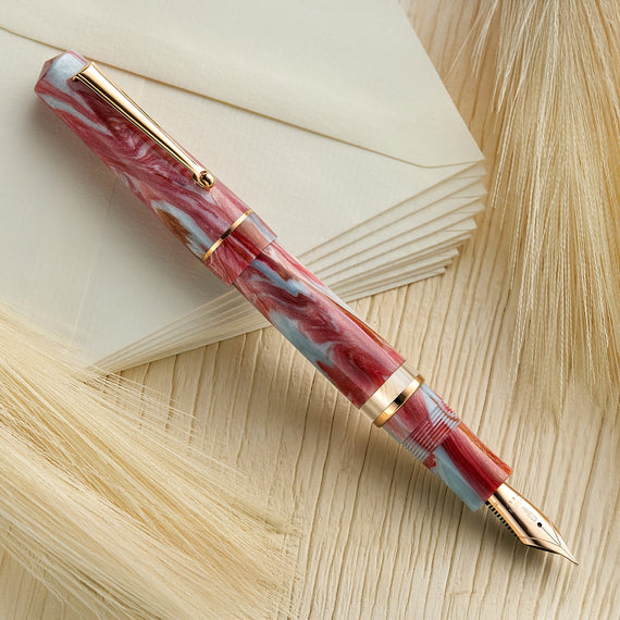 This image shows a fountain pen with a red and blue patterned body, rose gold trim, and conical tip.