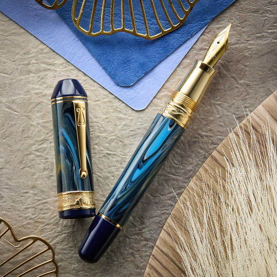 A fountain pen featuring a blue and gold swirled body with matching cap. There is a decorative gold band around the cap and at the top of the grip.