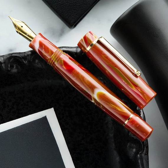 A red, gold, and white swirled resin fountain pen with gold trim.