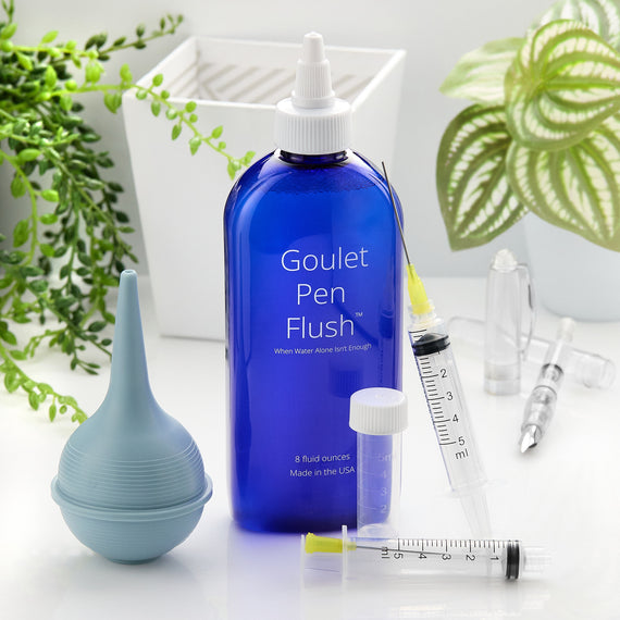 Blue Goulet Pen Flush bottle with accessories on a white surface with plants in the background