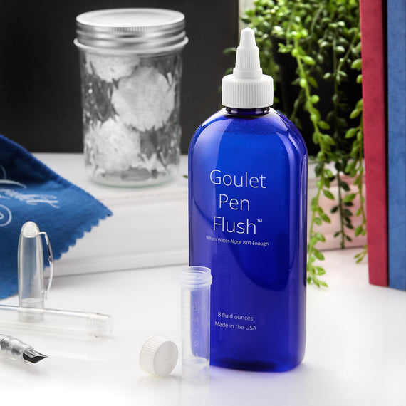 Blue bottle labeled 'Goulet Pen Flush' on a surface with stationery items.
