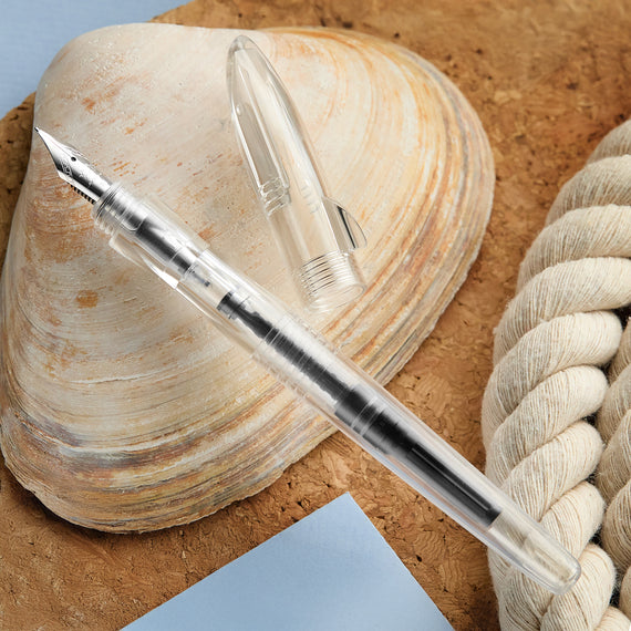 Clear pen on a shell with a woven rope and blue paper in the background