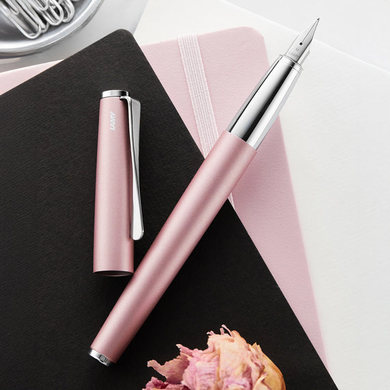 Pink pen with silver accents on a black surface with a pink flower and notebook.