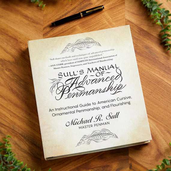 Book titled 'Sull's Manual of Advanced Penmanship' on a wooden surface with a pen and plants.