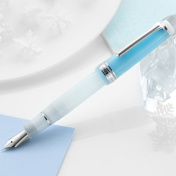 Light blue fountain pen on a white surface with a glass of water and a white plate in the background.