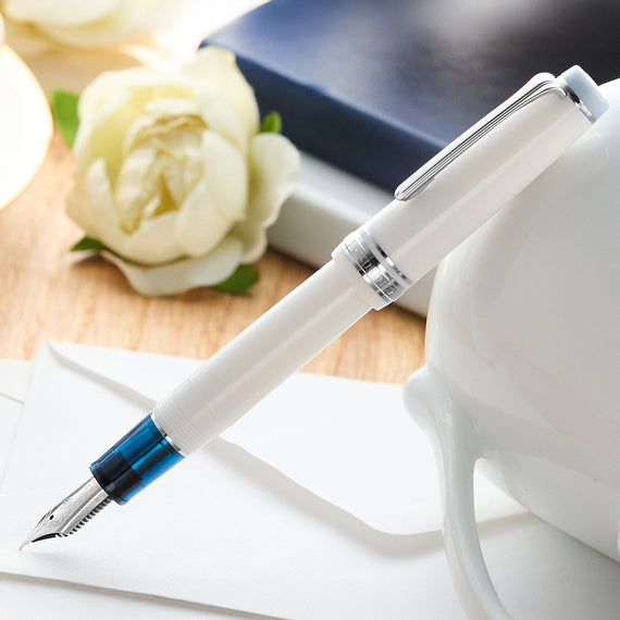 Fountain pen with a blue grip on a wooden surface with flowers and a notebook.