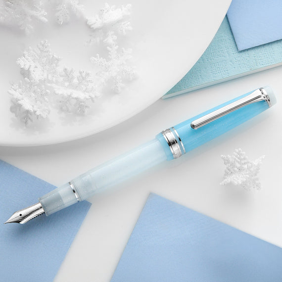 Light blue fountain pen with silver accents on a white surface with blue paper and snowflake decorations.