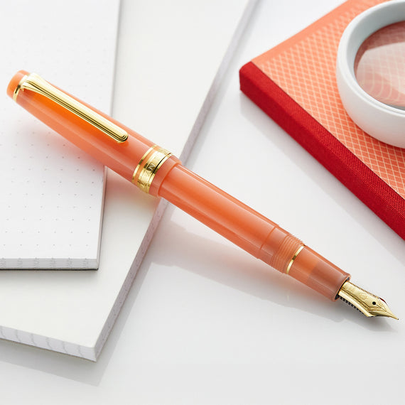 Orange fountain pen with gold accents on a white surface