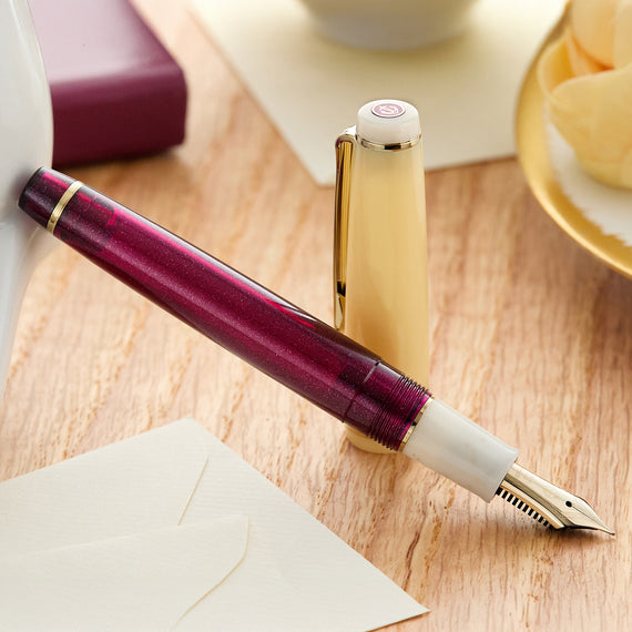 Fountain pen with a maroon body and white accents on a wooden surface.