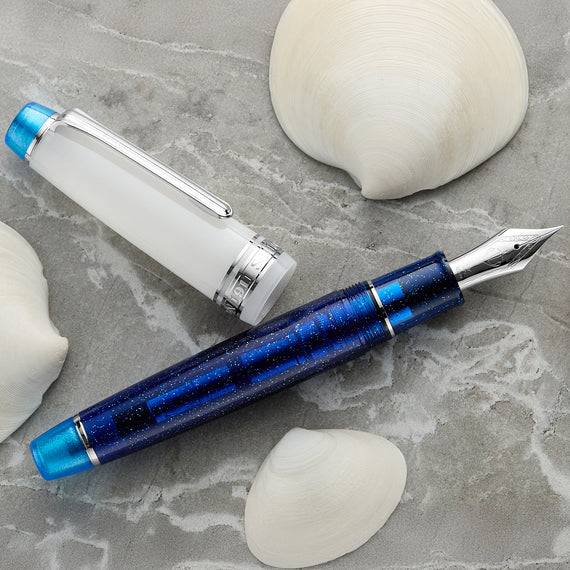 Blue and silver fountain pen on a gray surface with seashells