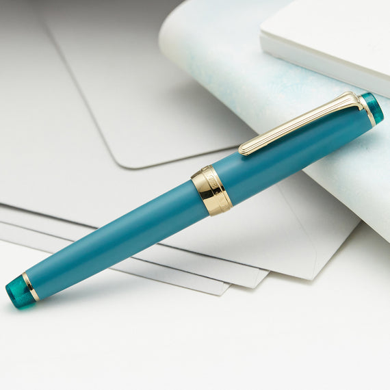 Teal pen with gold accents on a white surface
