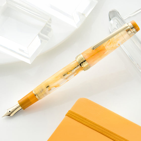 Fountain pen with a decorative cap on a white surface next to a yellow notebook.