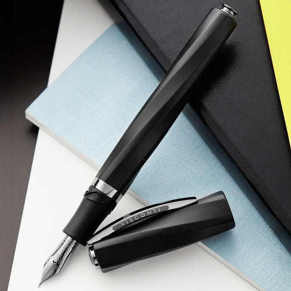 Black fountain pen with silver accents on a stack of notebooks
