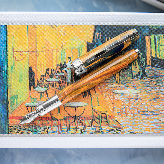 A fountain pen with silver accents on a painting of a café scene by Van Gogh.