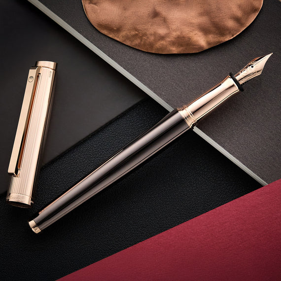 Rose gold fountain pen on a dark surface with a metallic disc