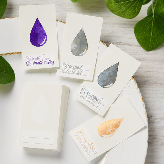 Set of cards with watercolor drop designs on a wooden surface with leaves.